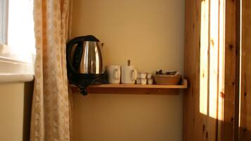 Una zona de cocina con un hervidor, tazas y un bol sobre un estante de madera.