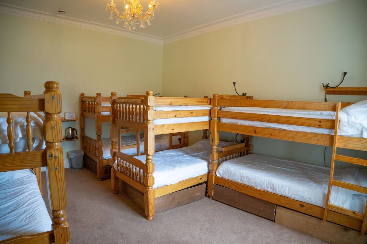 A room with four wooden bunk beds, a chandelier, and a small table with a kettle.