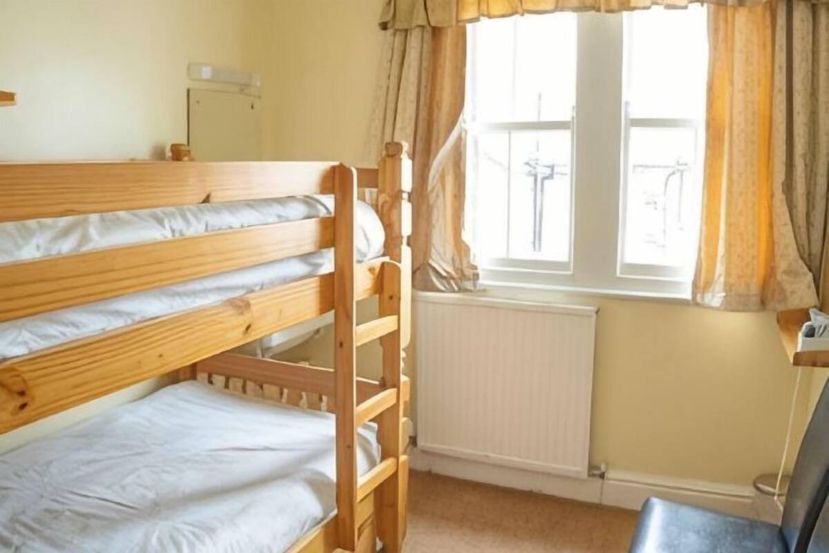 A bunk bed room with a window, radiator, and a chair.