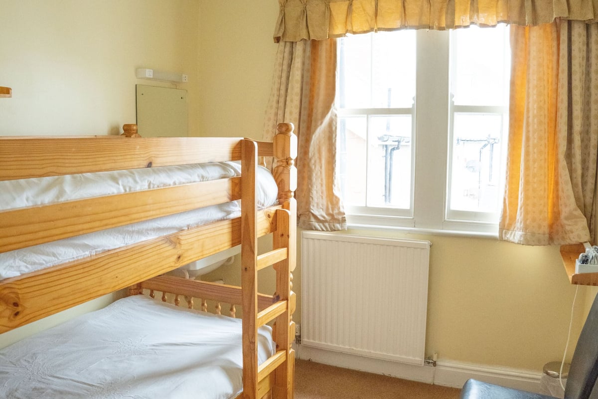 A room with bunk beds, a chair, a radiator, a window with curtains, and a chandelier.