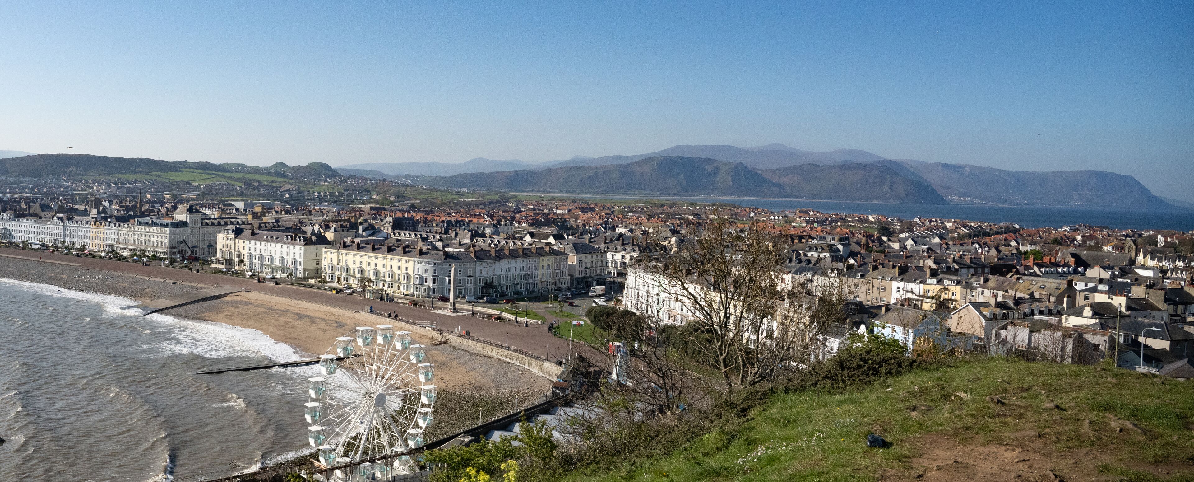 A coastal town with a prominent Ferris wheel, a beach, and a mountainous backdrop.