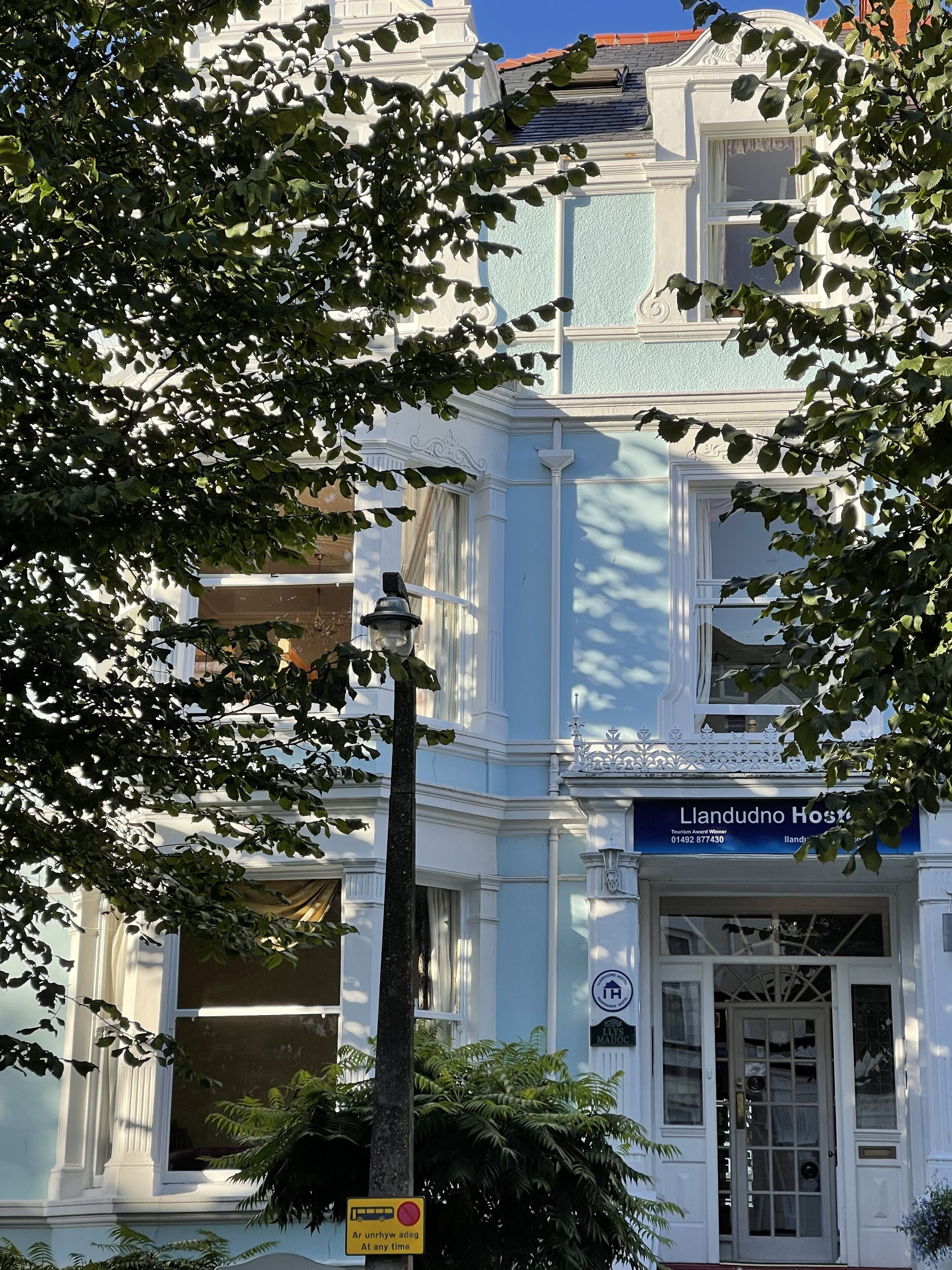 Un edificio con un letrero que dice "Llandudno Host". Presenta un estilo arquitectónico tradicional con detalles ornamentales y una entrada destacada.