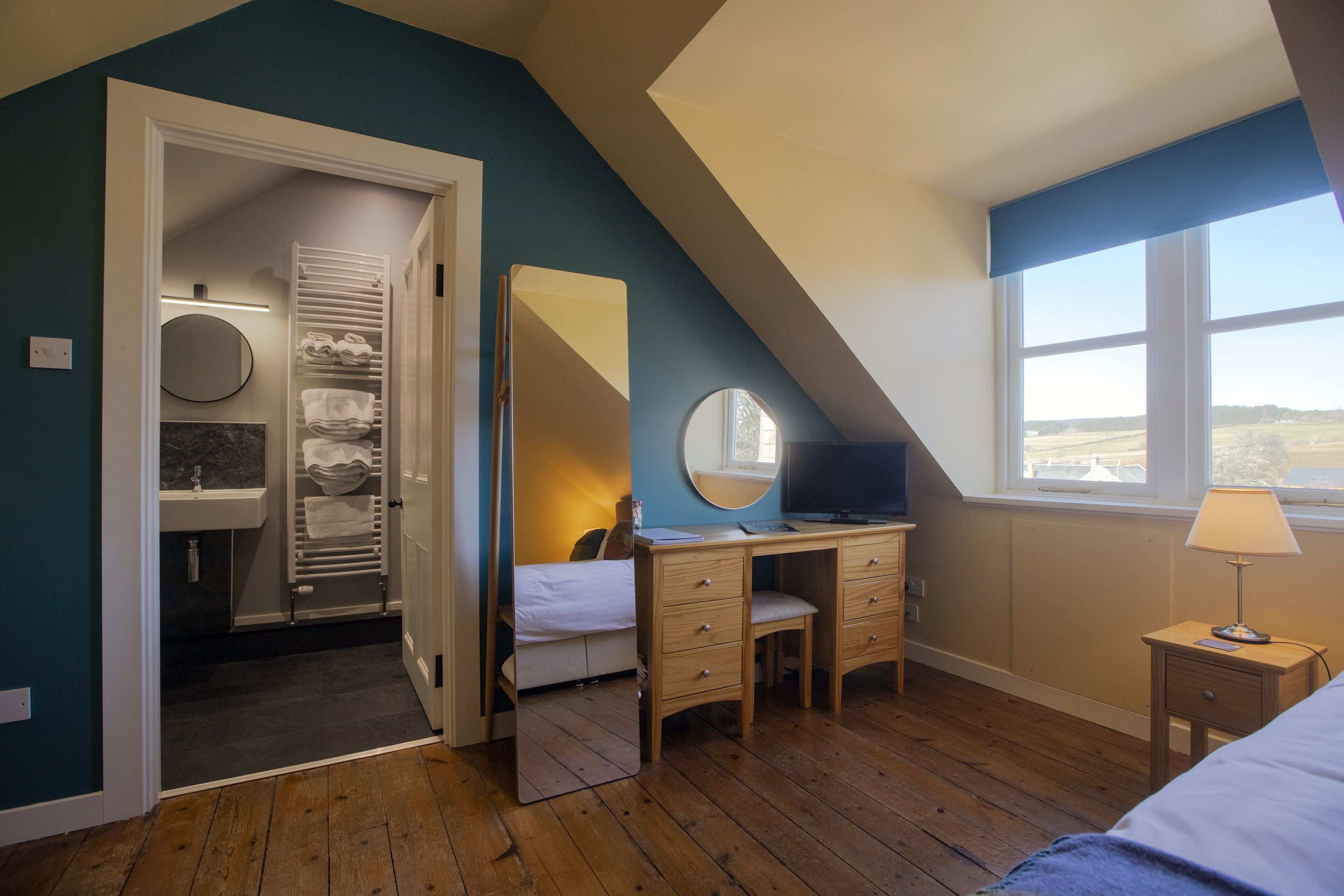 Un dormitorio con un escritorio de madera, una cama, un espejo y una ventana con vistas.