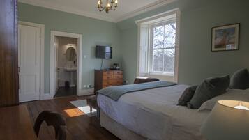 A bedroom with a large bed, a television, a dresser, and a window.