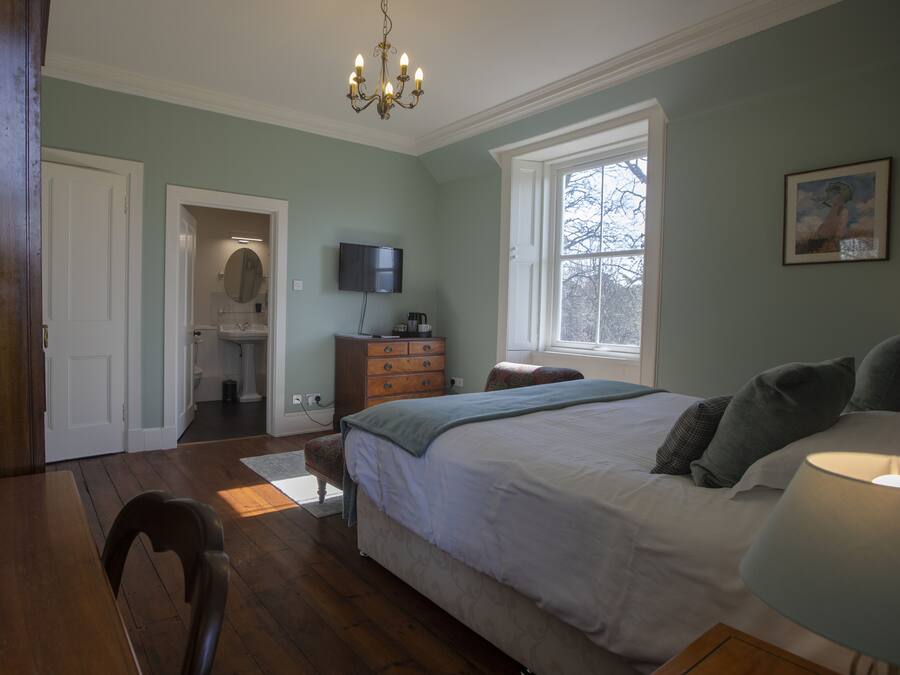 A bedroom with a large bed, a television, a dresser, and a window.