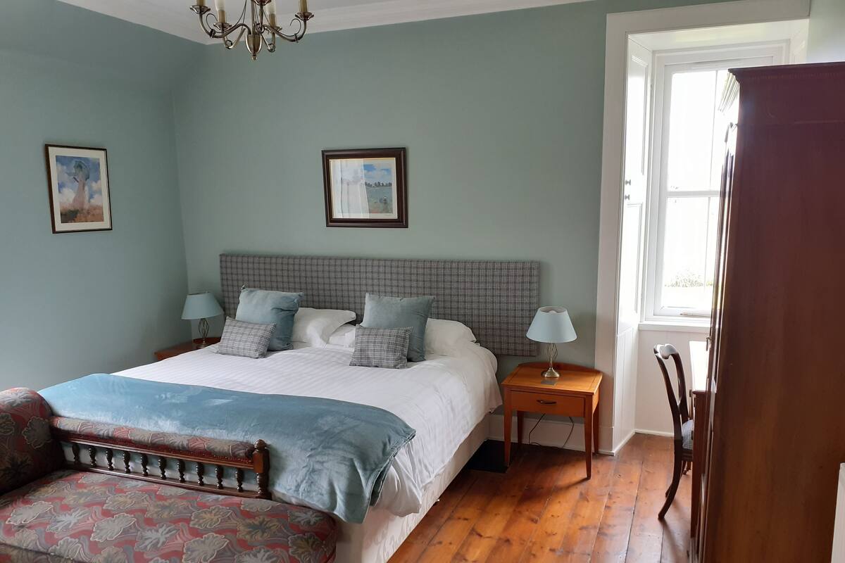 A bedroom with a large bed, two bedside tables, a bench, and a window.