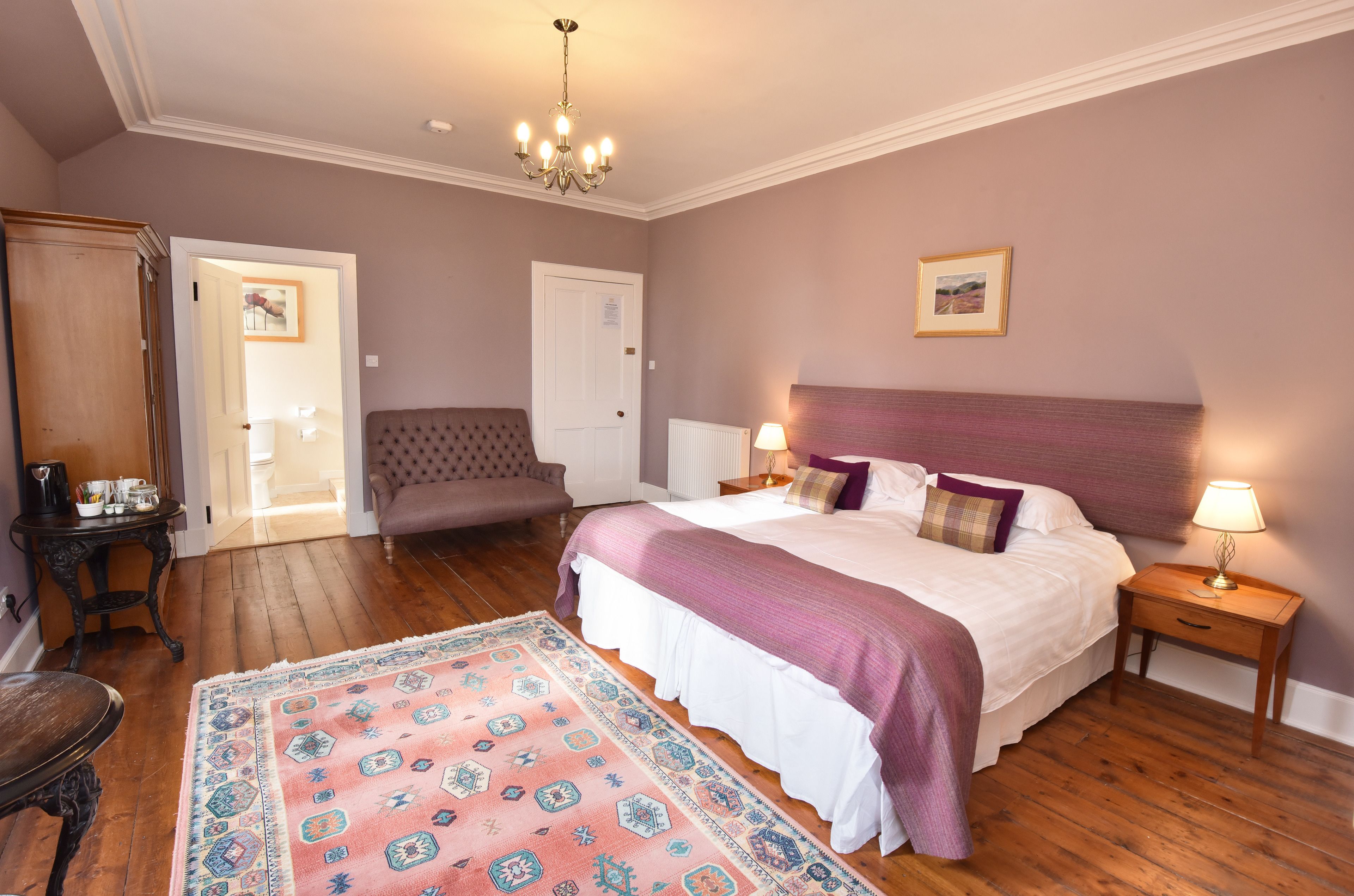 A bedroom with a large bed, a bedside table with a lamp, a chair, a dresser, and a rug.