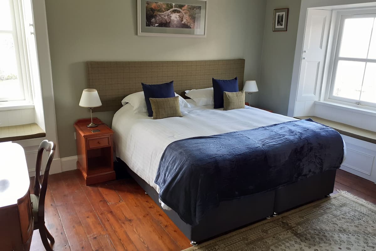 A neatly arranged bedroom with a large bed, a bedside table with a lamp, a chair, and a rug.