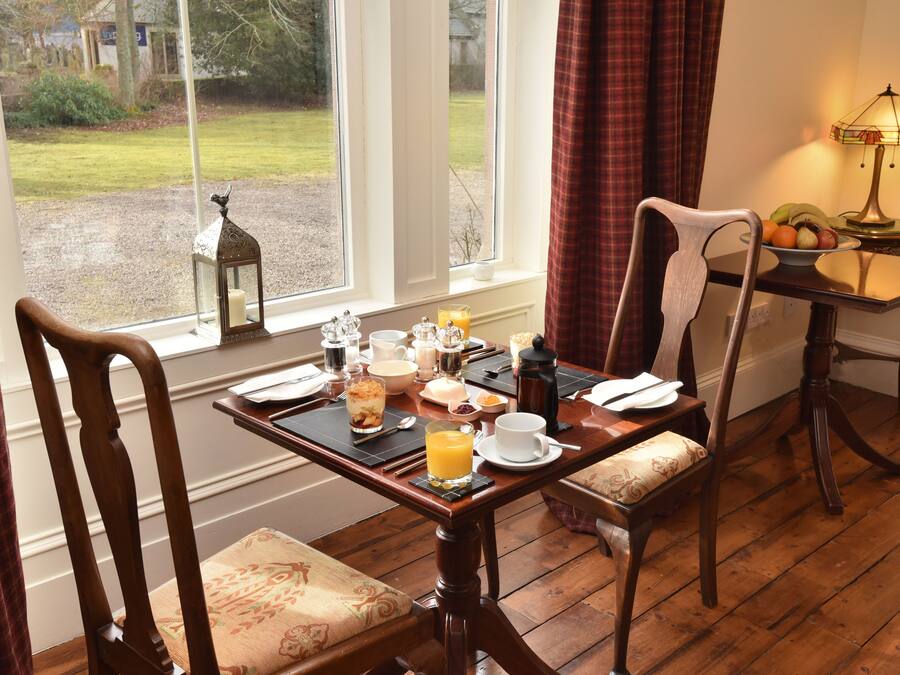 A dining table set with breakfast items, a view of the garden through the window, and a lamp on the side table.