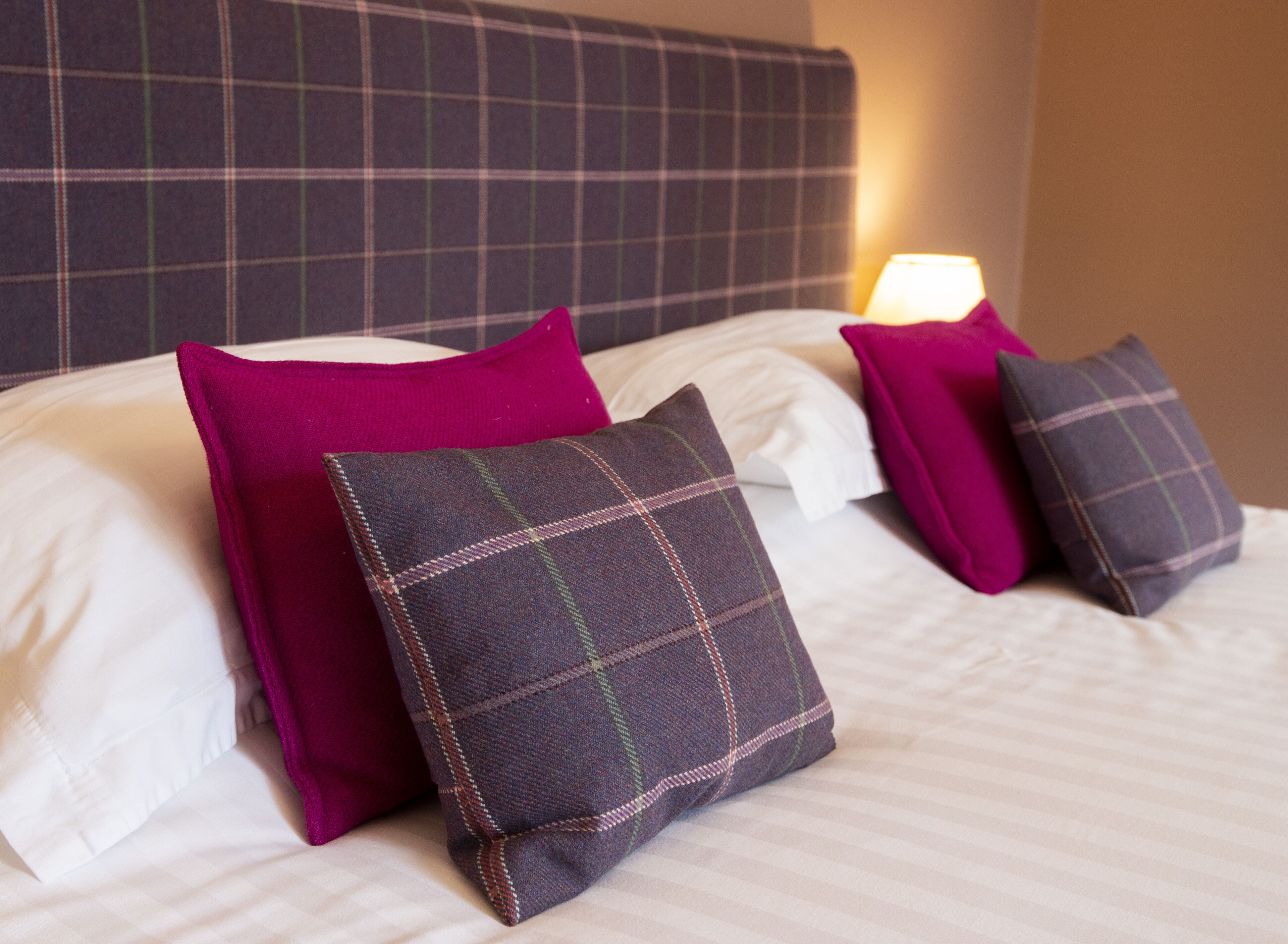 A neatly made bed with a plaid-patterned pillow and a bright pink pillow.