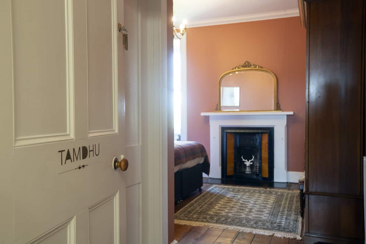 A room with a fireplace, a bed, and a door labeled "TAMDHU".
