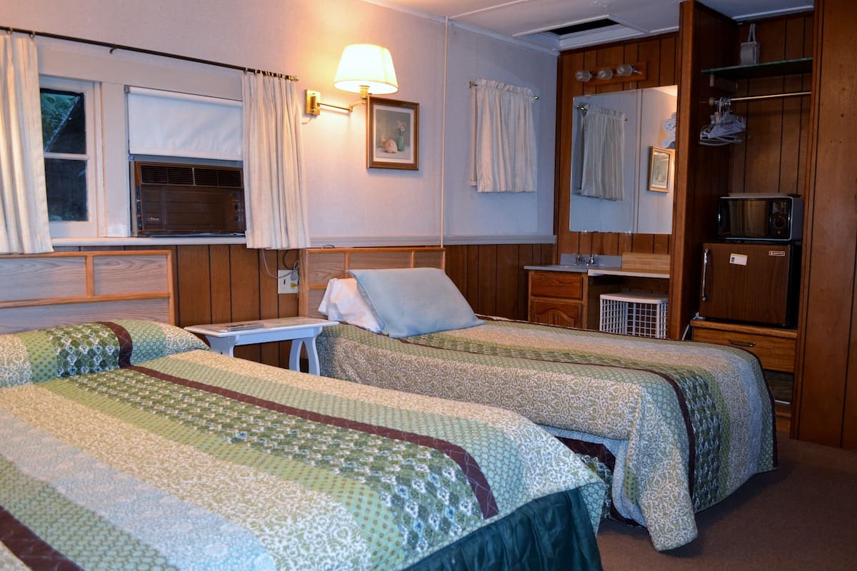 A room with two beds, a small table, a lamp, a microwave, and a refrigerator.