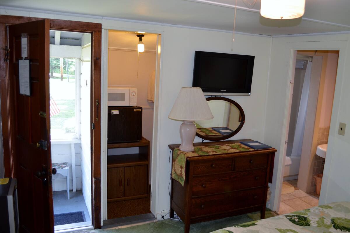 A bedroom with a wooden dresser, a television mounted on the wall, and a door leading to a bathroom.