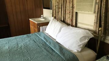 A bedroom with a bed, a nightstand, a dresser, a window with curtains, and an air conditioning unit.