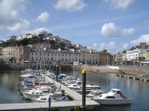 A marina with boats docked, a waterfront promenade, and buildings in the background. - Tusker Lodge (Torquay)