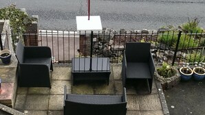 An outdoor patio with black wicker furniture, a stone floor, and a metal fence. - Tusker Lodge (Torquay)