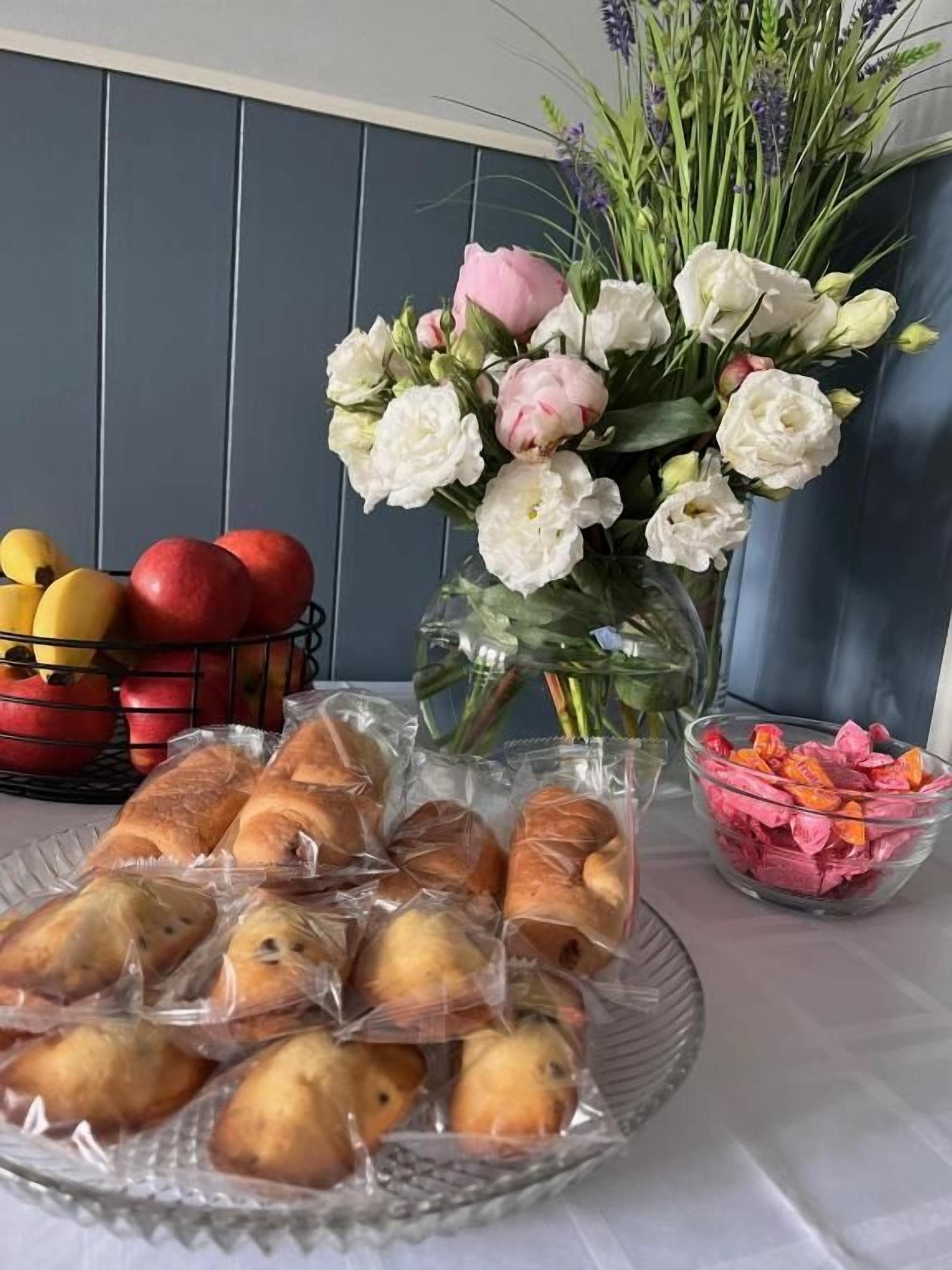 A table with pastries, a vase of flowers, and a bowl of fruit.