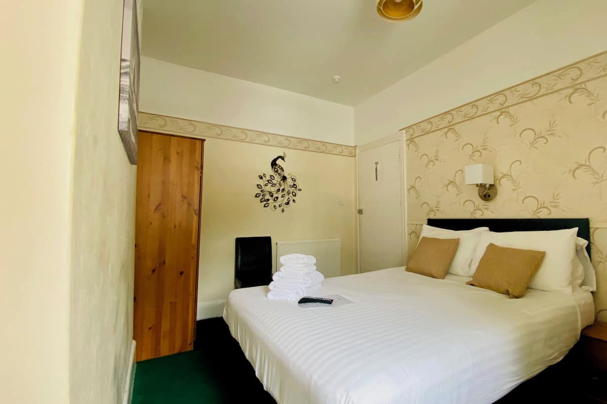A hotel room with a large bed, a wooden door, a wall decoration, and a bedside table with a lamp.