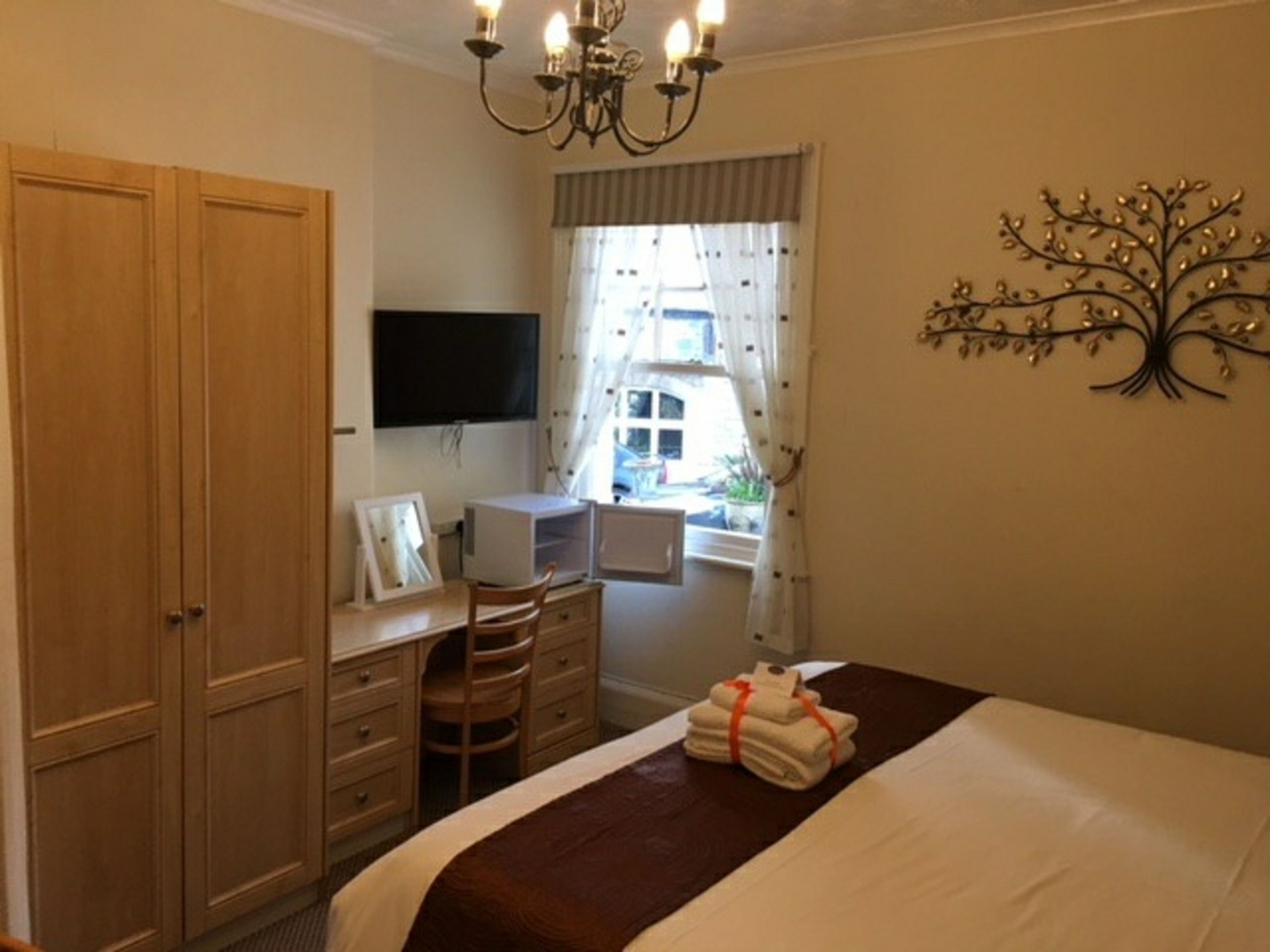 A bedroom with a bed, a desk with a computer, a TV, and a window with curtains.