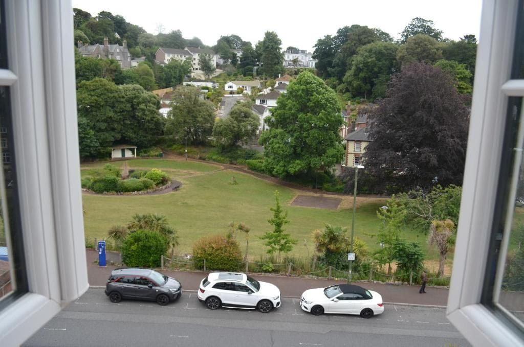A view of a residential area with houses, a grassy field, and parked cars.