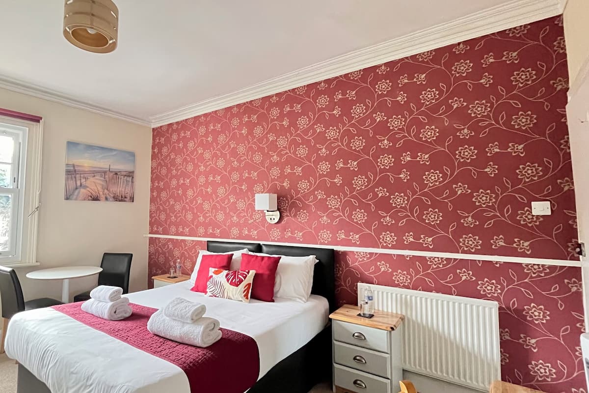 A bedroom with a bed, bedside tables, a chair, a window, and a radiator.
