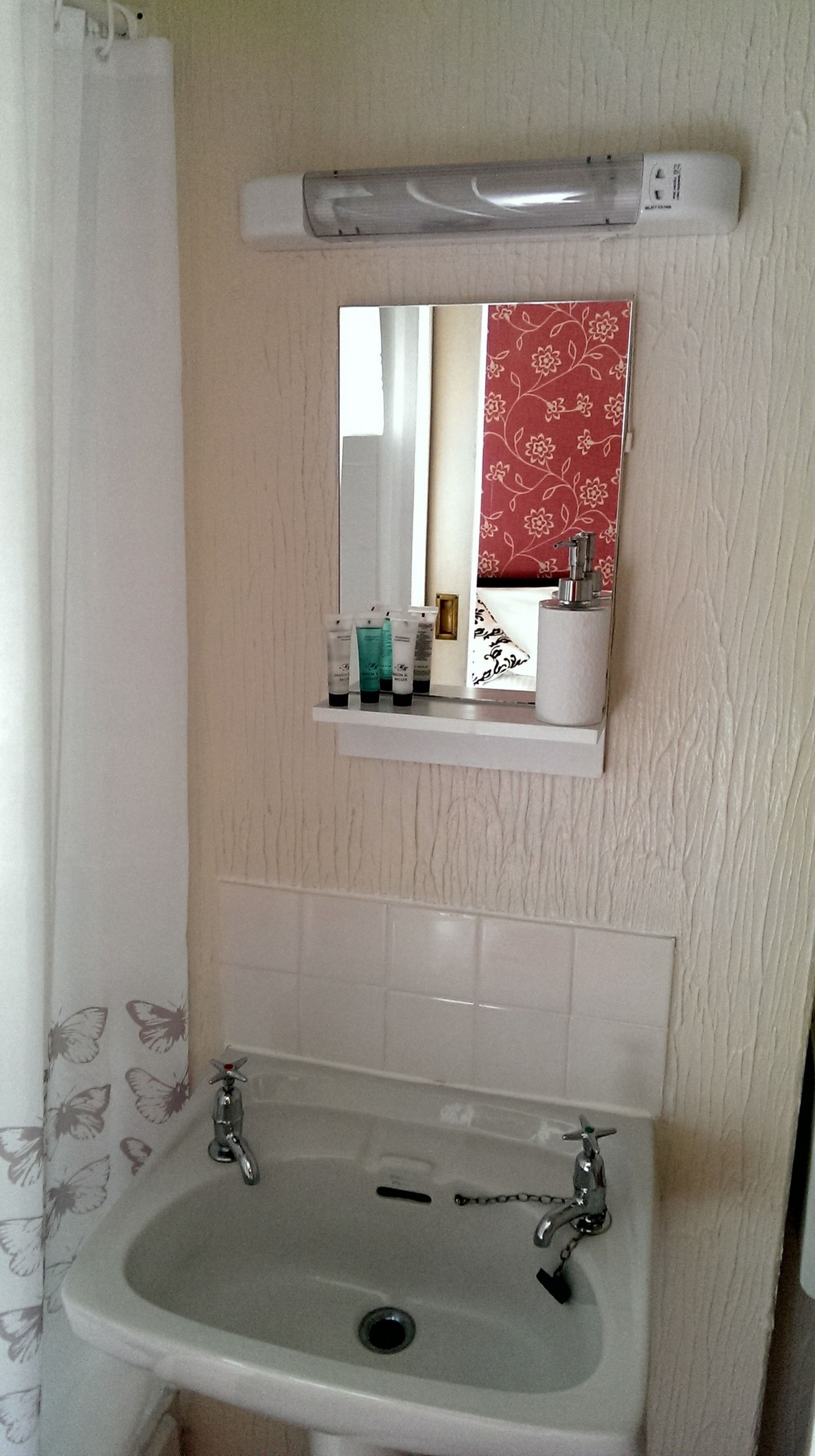 A bathroom with a white sink, a mirror above it, and a shelf with toiletries.