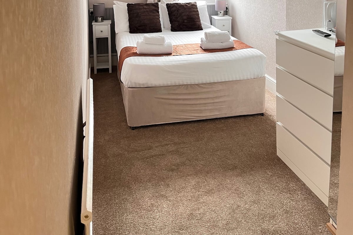 A neatly arranged bedroom with a bed, bedside tables, a TV, and a window with curtains.