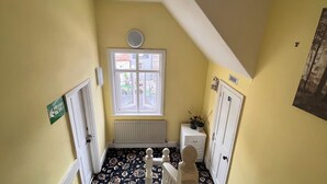 A narrow hallway with a window, a radiator, a white radiator cover, a white door, and a green sign on the wall. - Tusker Lodge (Torquay)