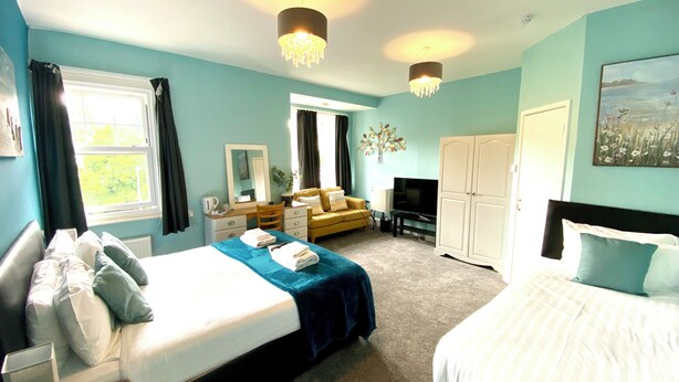 A hotel room with a bed, a sofa, a TV, a wardrobe, and a desk. - Tusker Lodge (Torquay)