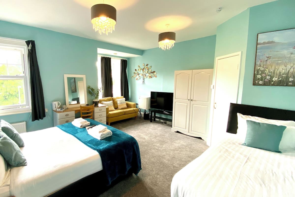 A hotel room with a bed, a sofa, a TV, a wardrobe, and a desk.