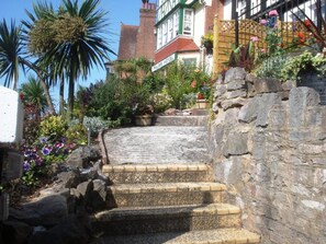 A staircase leading to a hotel entrance with a stone wall on one side and a variety of plants and flowers. - Tusker Lodge (Torquay)