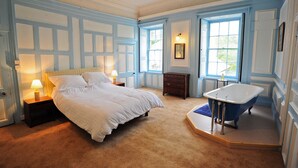 A bedroom with a bed, a dresser, a vanity, and a bathtub. - Kelly House (Lifton)