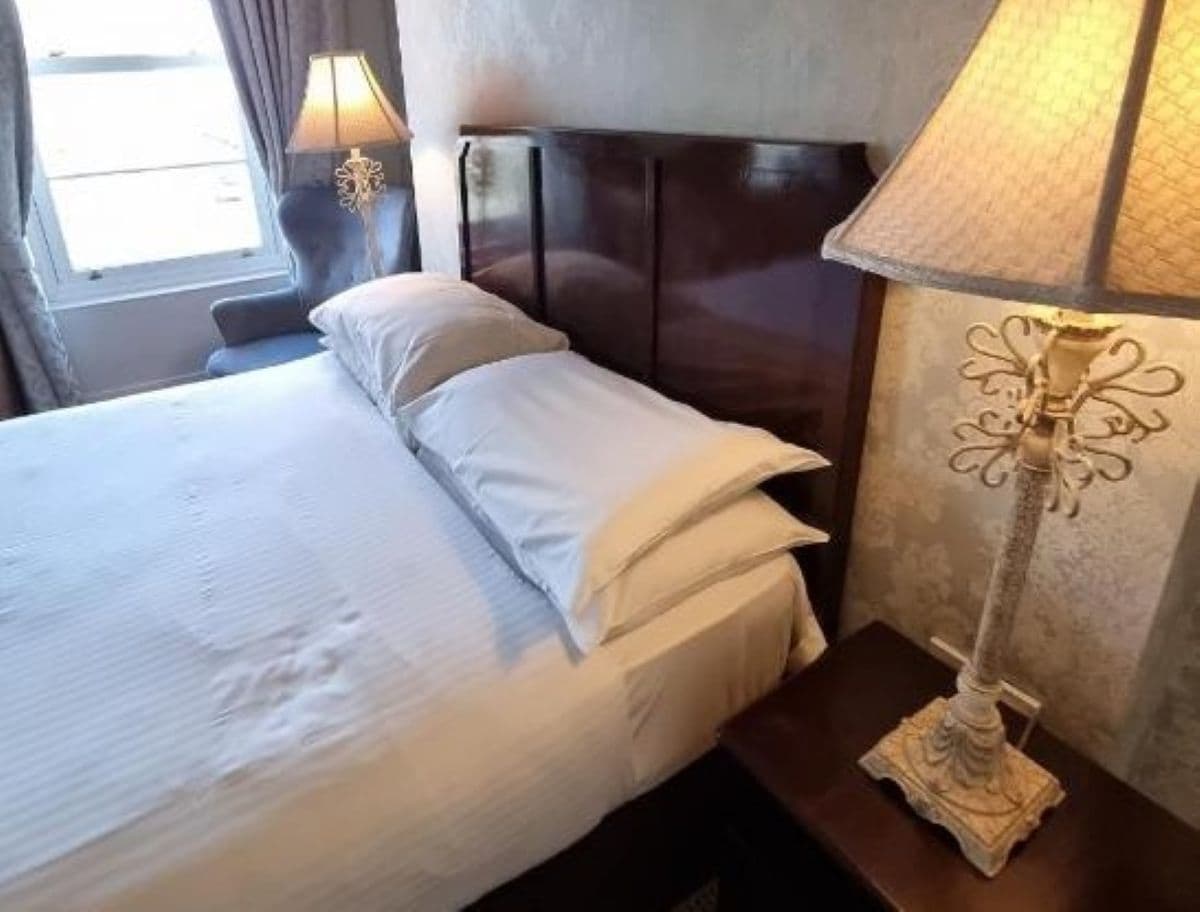 A hotel room with a bed, two bedside lamps, and a window.