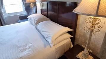 A hotel room with a bed, two bedside lamps, and a window.