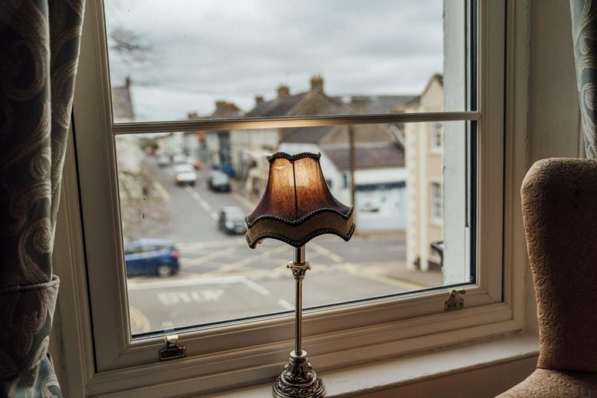 Een lamp op een vensterbank met uitzicht op een straat.