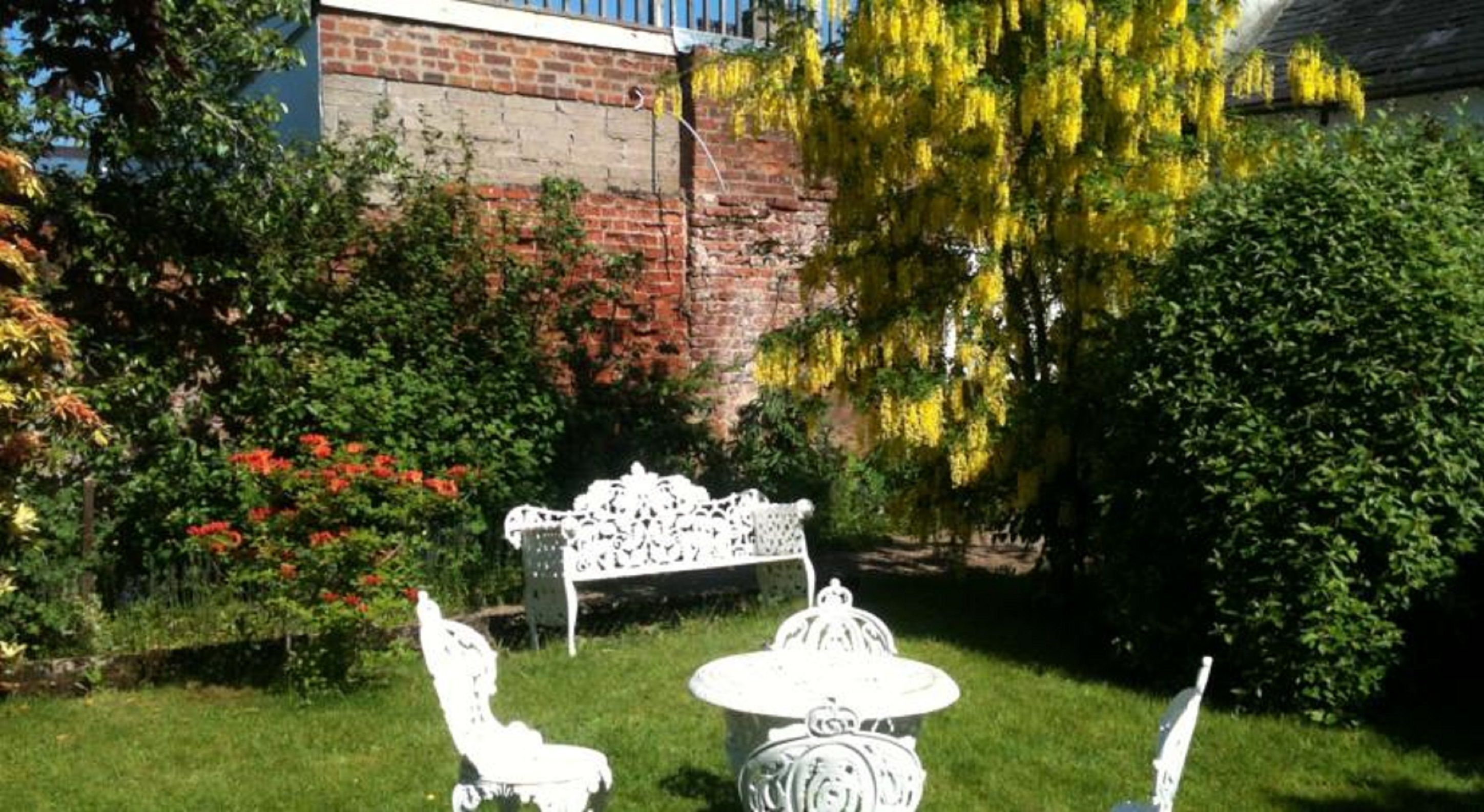 Un giardino con una panchina, un tavolo e una sedia, tutti e tre di colore bianco.