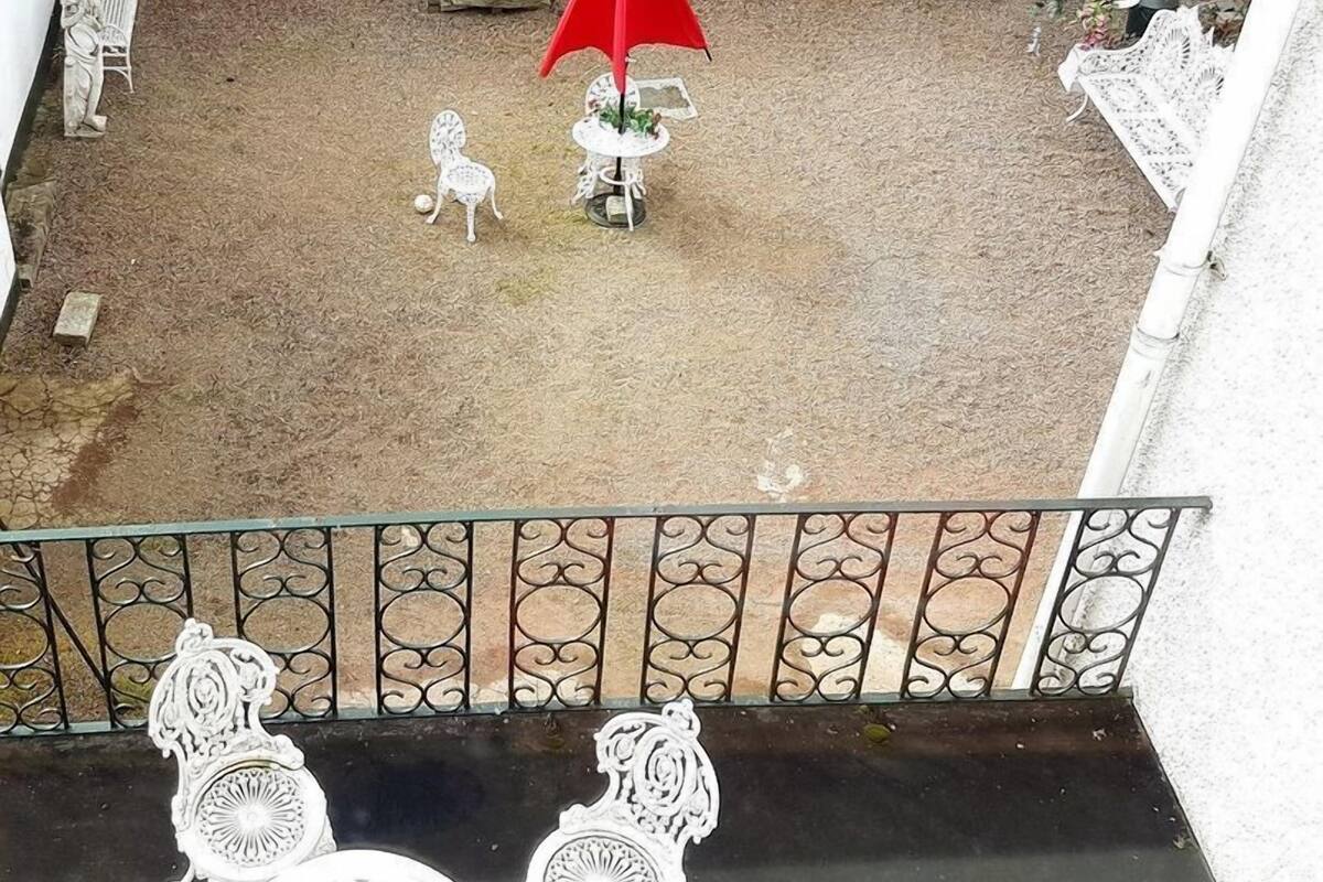 A courtyard with a red umbrella, white chairs, and a white building with red doors and windows.