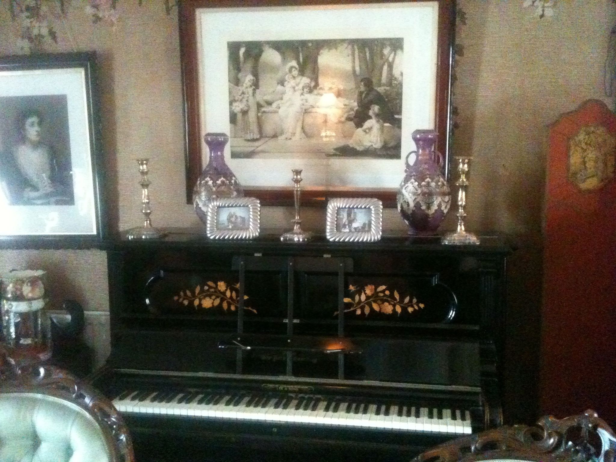 A piano with decorative vases and framed pictures on a stand.