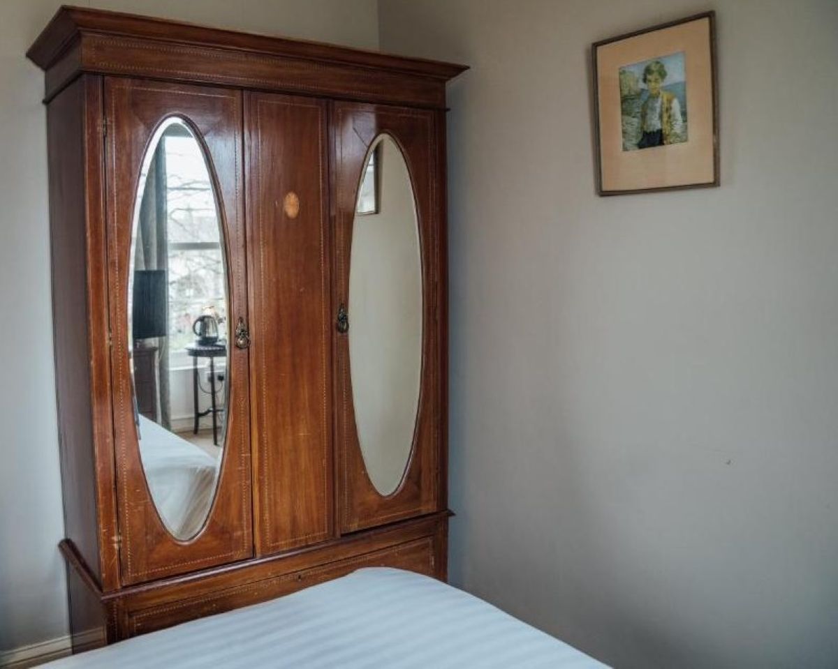 Een slaapkamer met een houten garderobe, een bed en een ingelijst kunstwerk aan de muur.