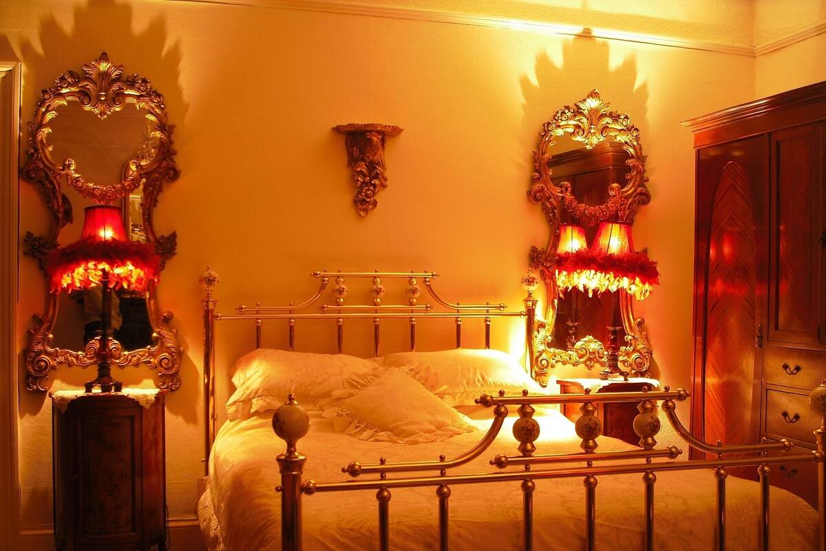 A bedroom with a bed, ornate mirrors, and a nightstand.