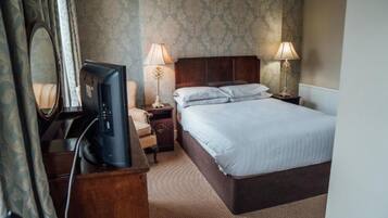 Quarto de hotel com cama, televisão, mesa de cabeceira e luminária.