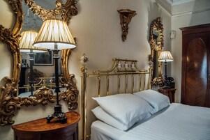 Una habitación de hotel con una cama, una mesita de noche, una lámpara, un espejo y un radiador fijado a la pared.