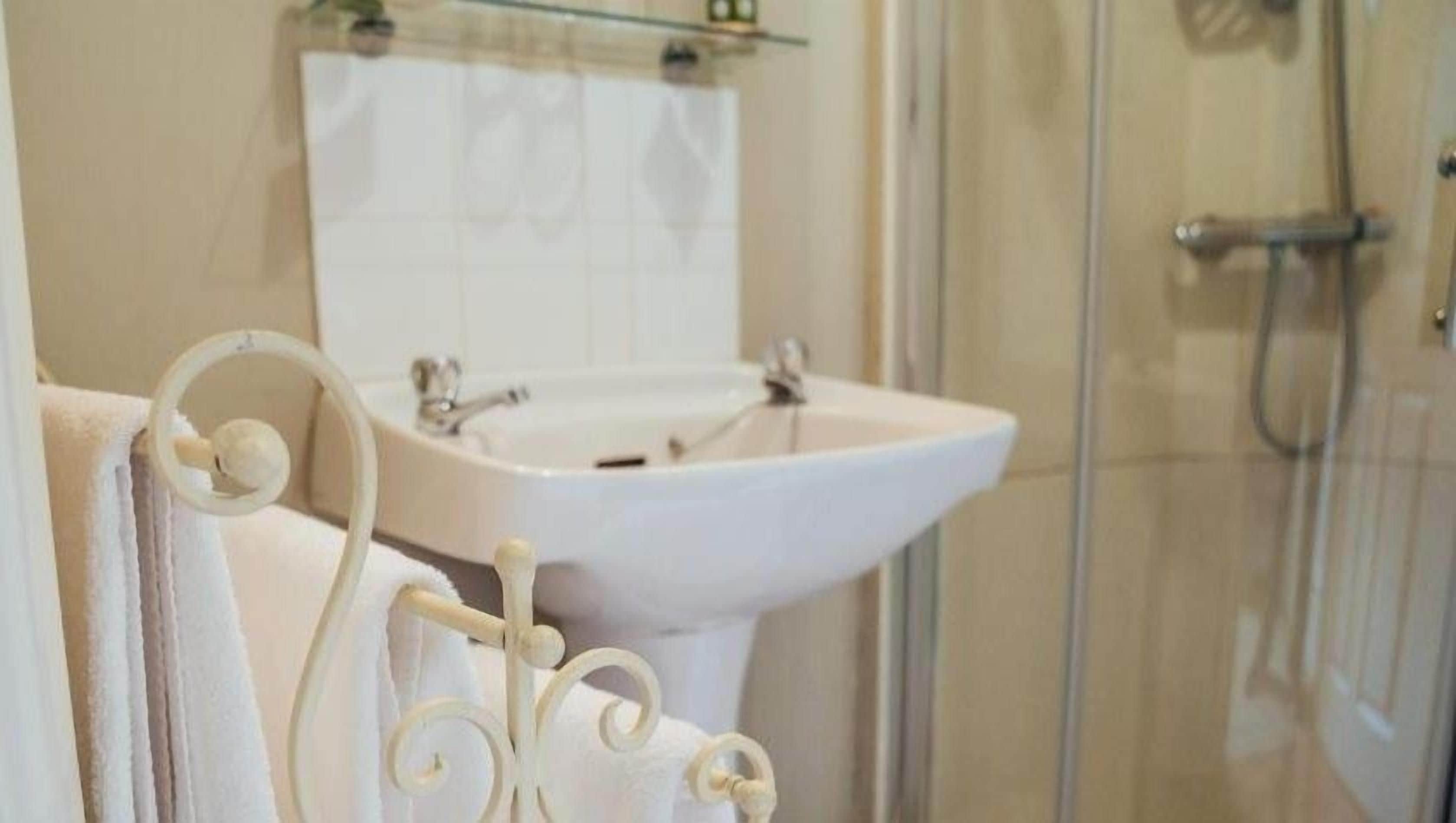 Un baño con lavamanos blanco, cabina de ducha con mampara de vidrio y un perchero para toallas.