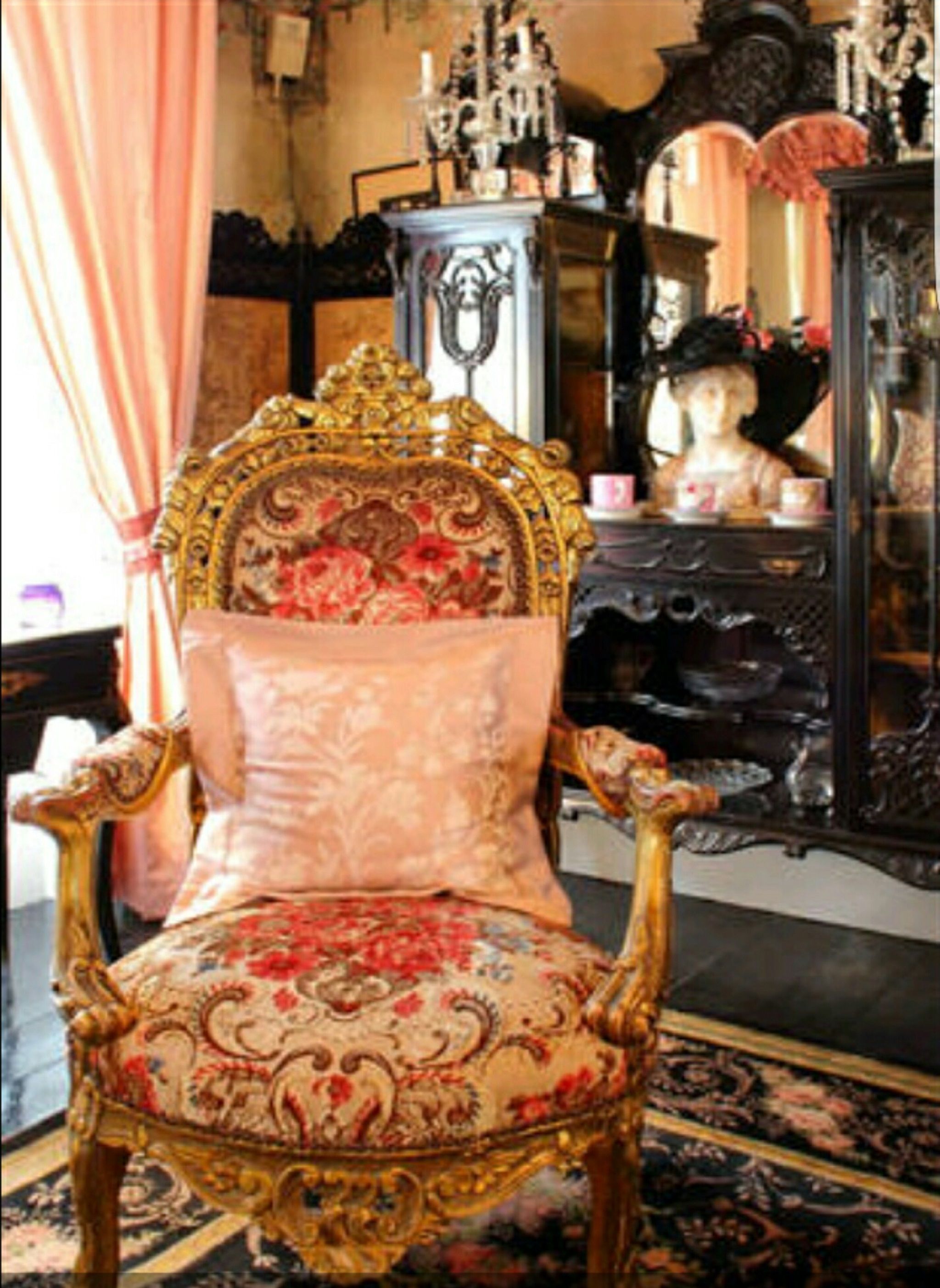 A richly decorated room with a large ornate chair, a mirror, and a dresser.