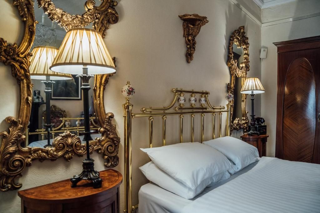 Een hotelkamer met een bed, sierlijke spiegel met gouden lijst en een klassieke houten garderobekast.