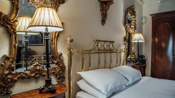 Een hotelkamer met een bed, sierlijke spiegel met gouden lijst en een klassieke houten garderobekast.