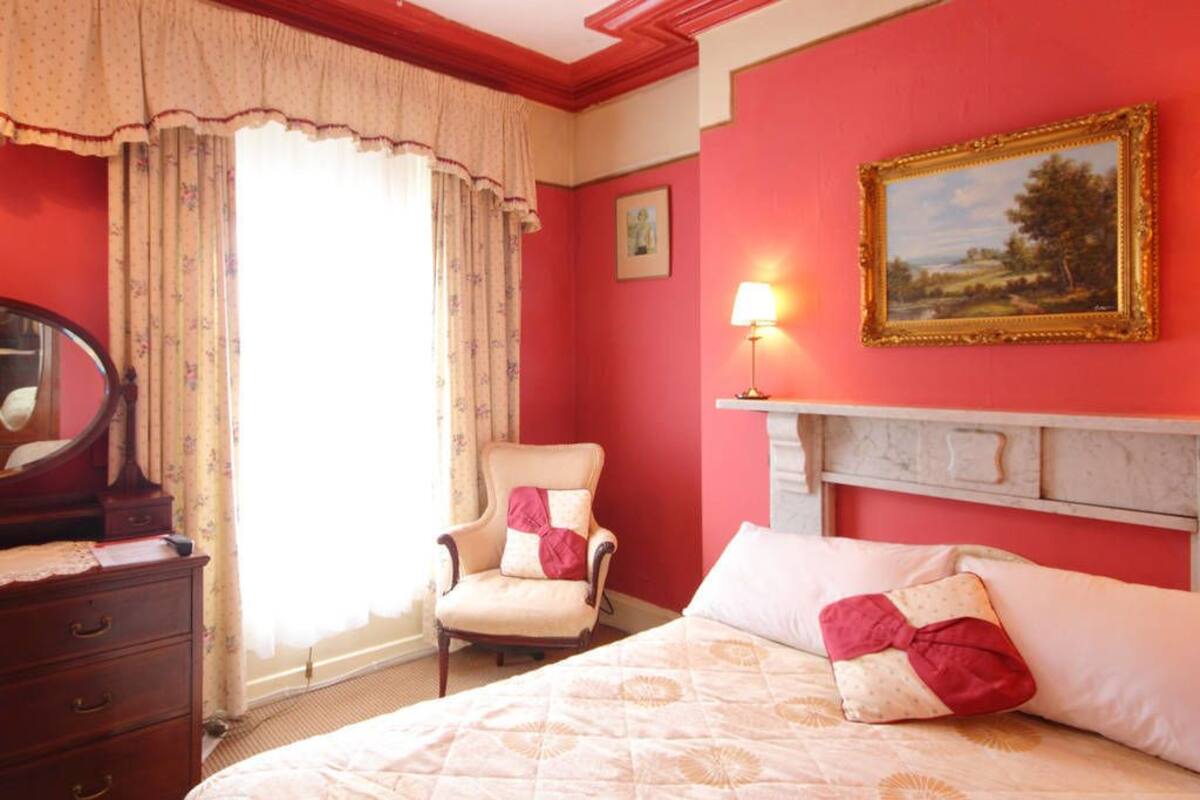 A hotel room with a bed, a chair, a dresser, a mirror, a lamp, and a painting on the wall.