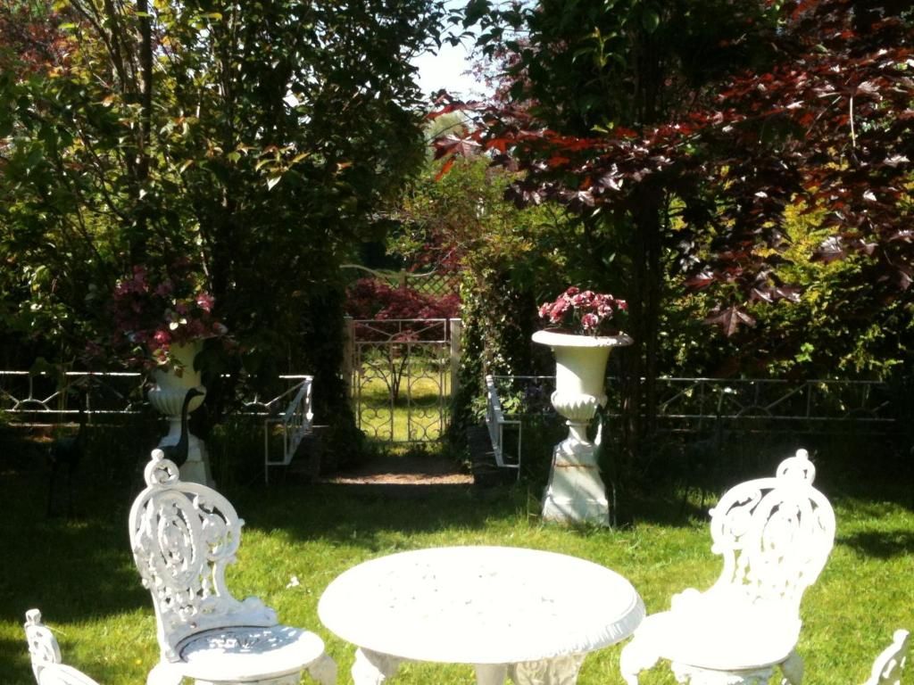 Un jardín con una mesa blanca y dos sillas, rodeado de follaje y una fuente decorativa.