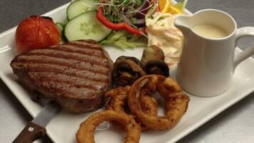 A plate with a steak, onion rings, a salad, and a cup of sauce.