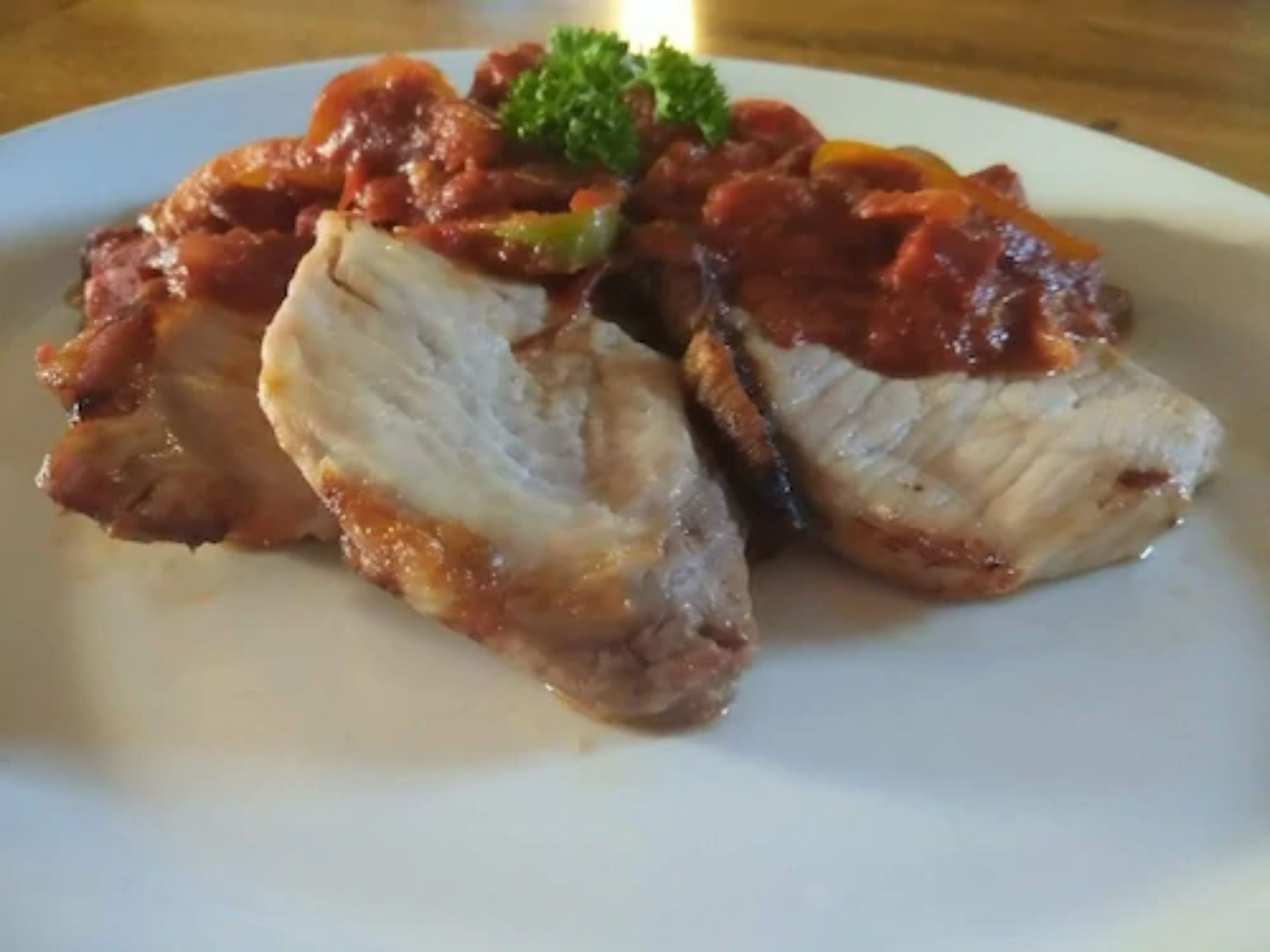 A plate of sliced meat with a tomato-based sauce and a garnish.